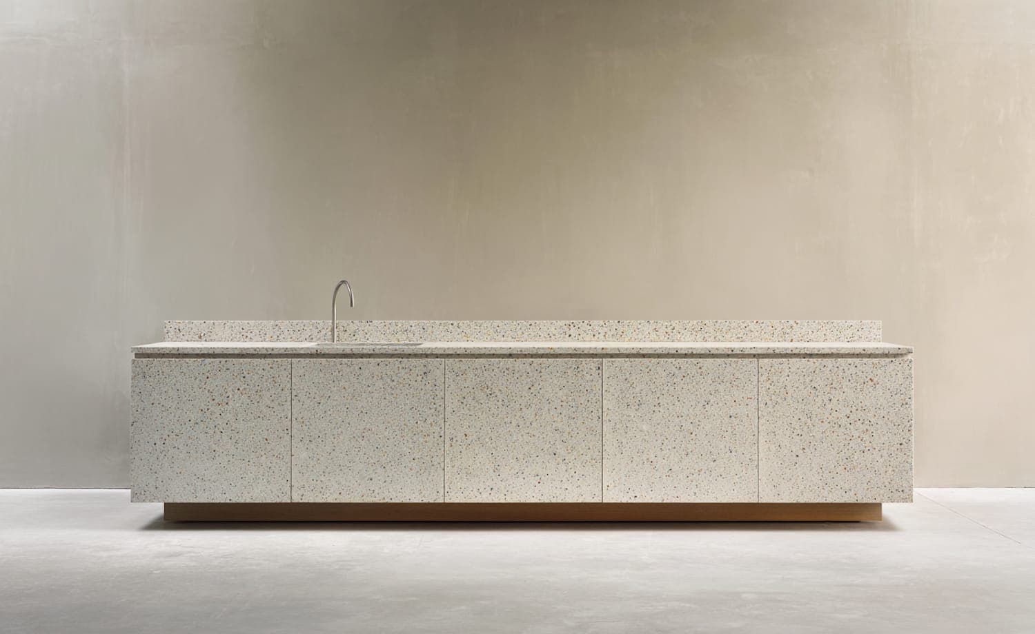 The kitchen island, a single terrazzo slab with a slim brushed-steel tap against a plain wall