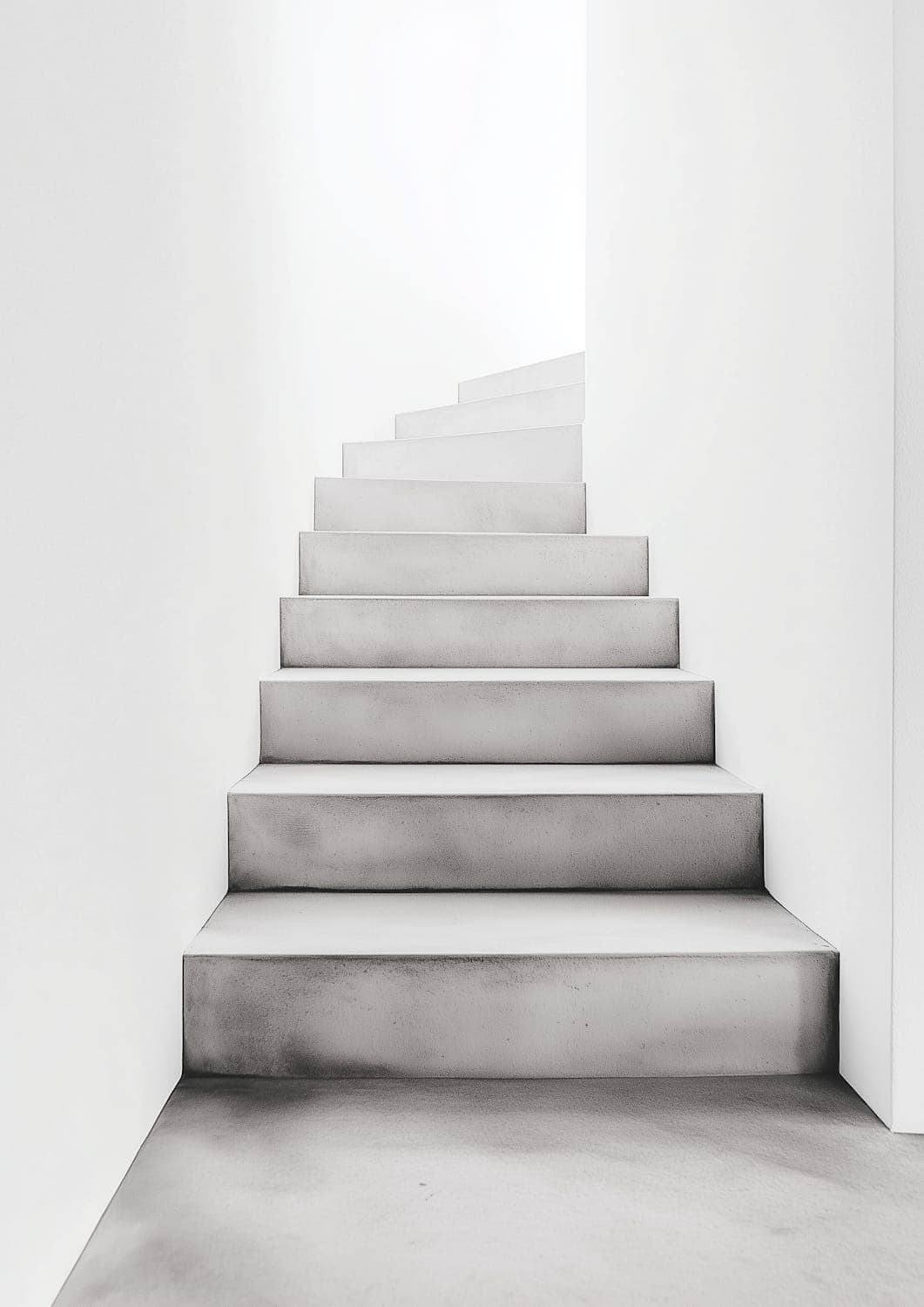 The in-situ concrete stair curving upward between white plastered walls under soft daylight