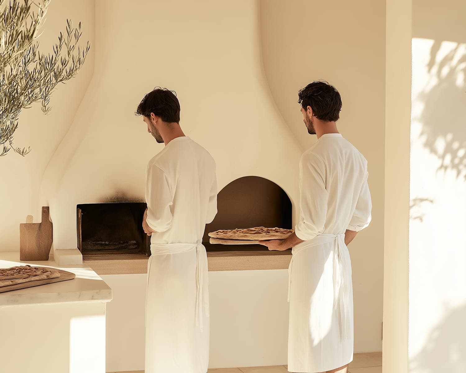Two chefs working at the open pass beside the wood-fired oven