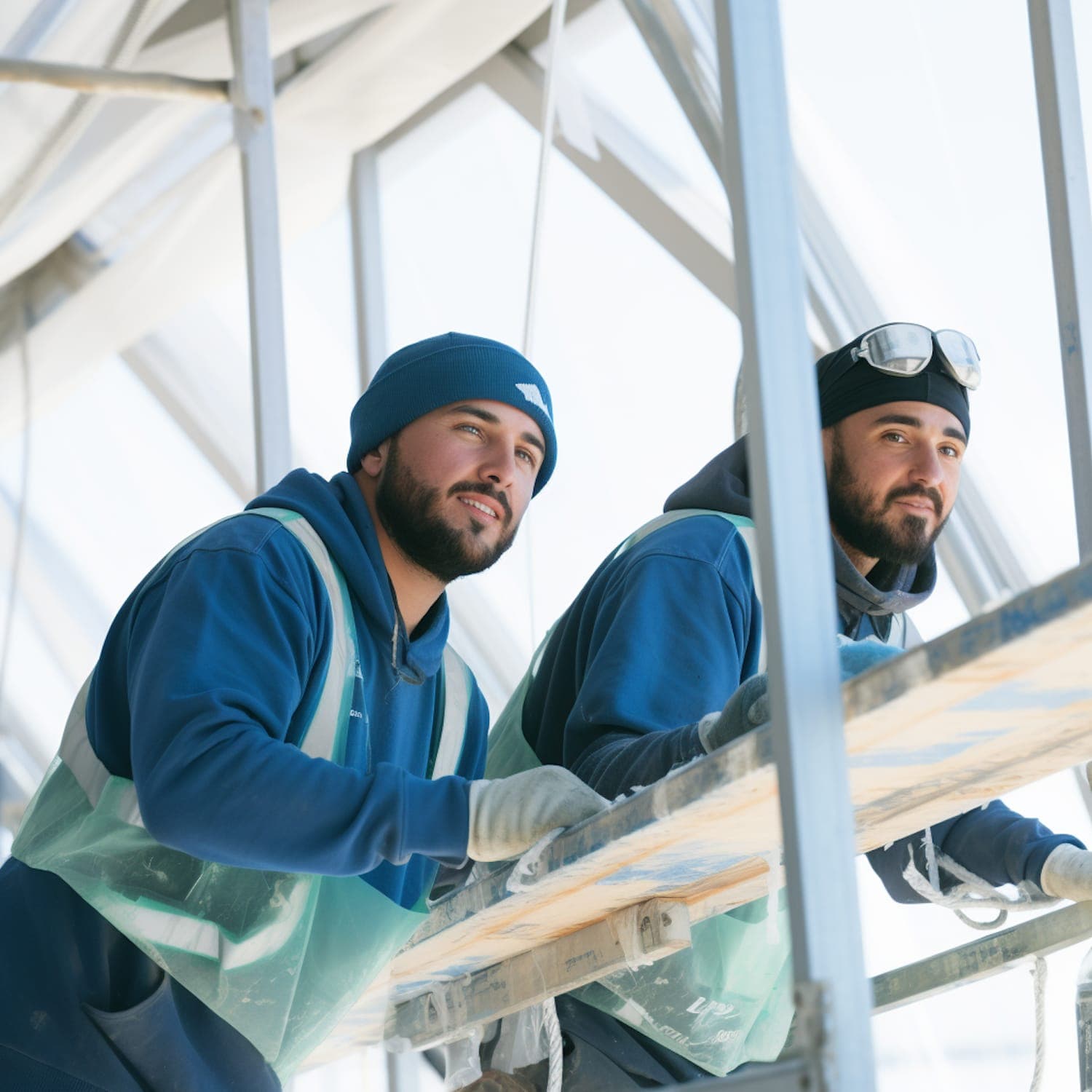 Two workers on scaffolding in high-visibility vests, working on a building facade